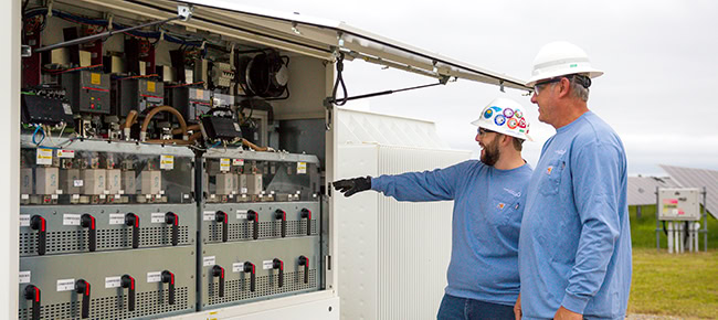 Two men look at the inside of a power inverter