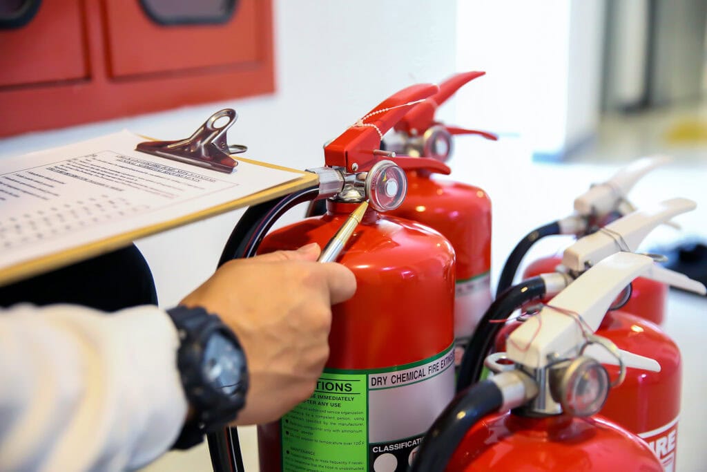 A hand and a clipboard are seen next to a set of fire extinguishers