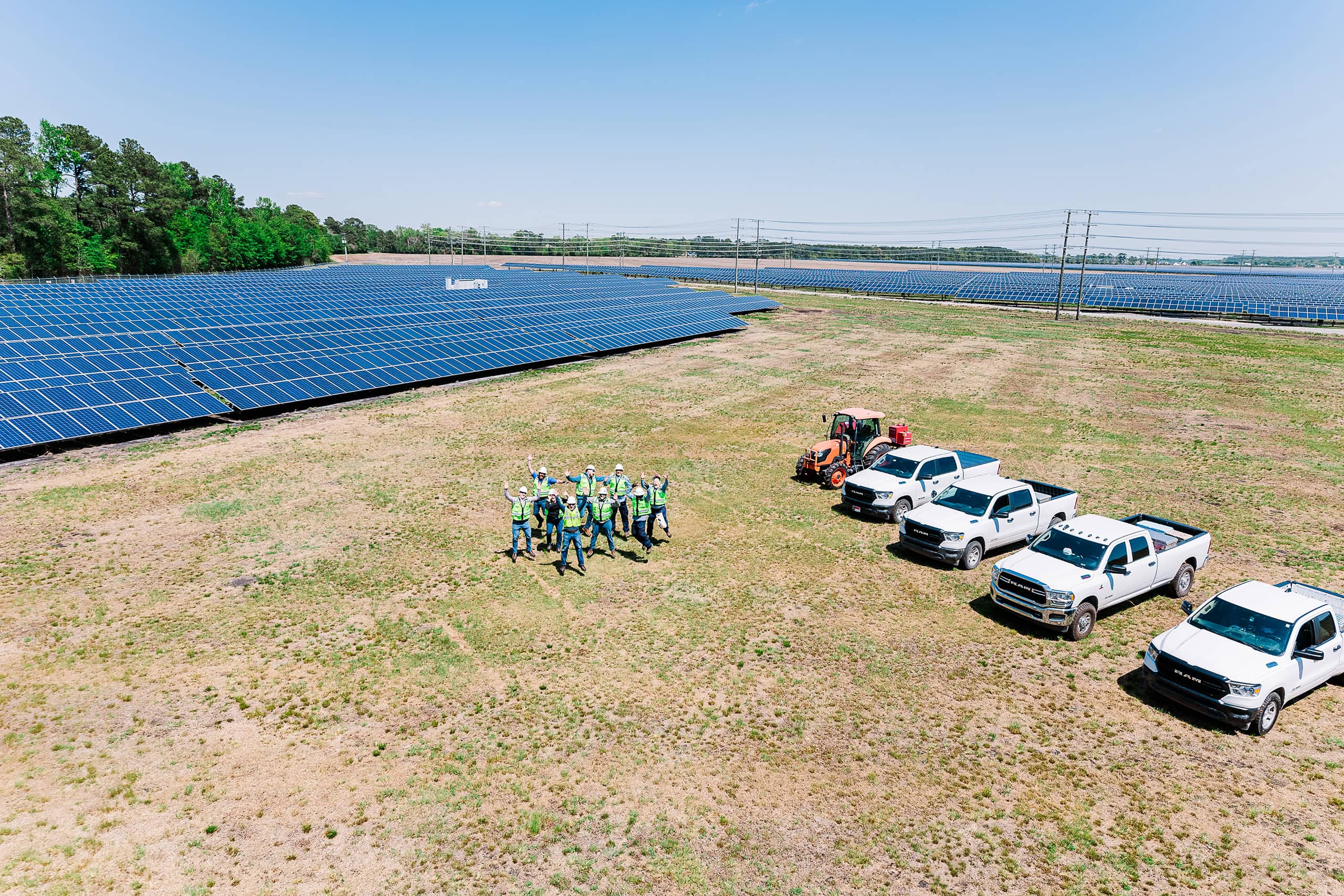 A group of people in safety vests leap into the air on a solar farm as seen from above