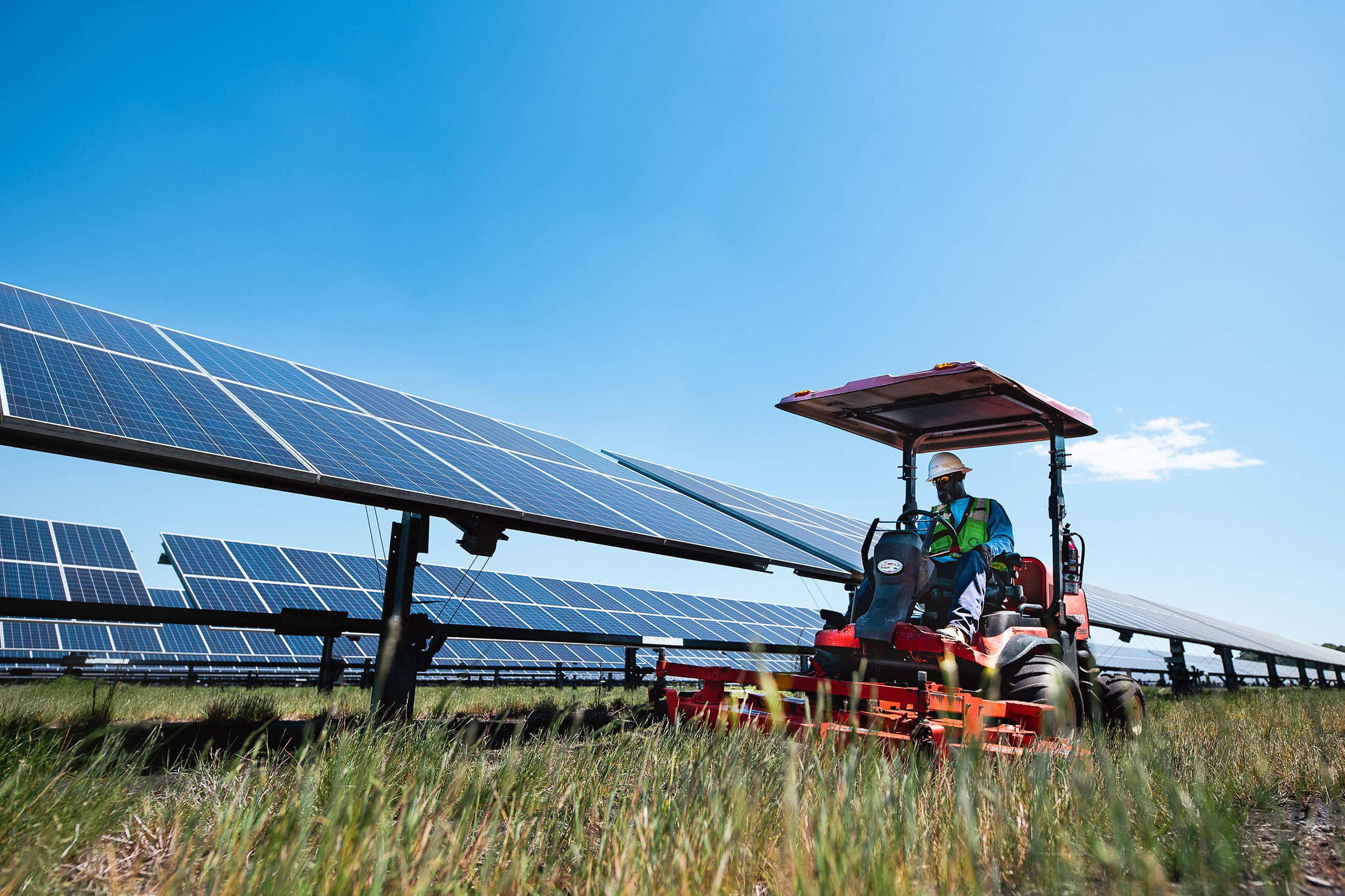 A man drives a tractor alongside a solar array