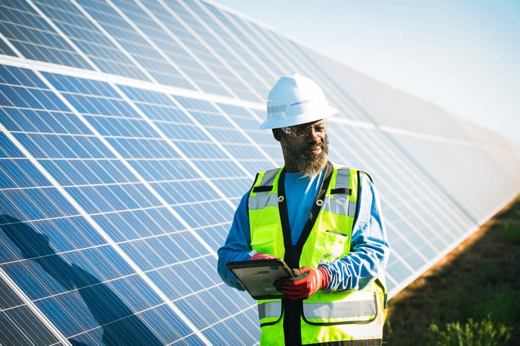 A man is safety gear stands next to a row of solar panels