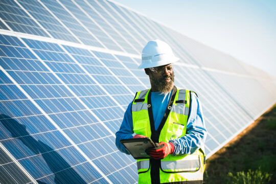 A man is safety gear stands next to a row of solar panels
