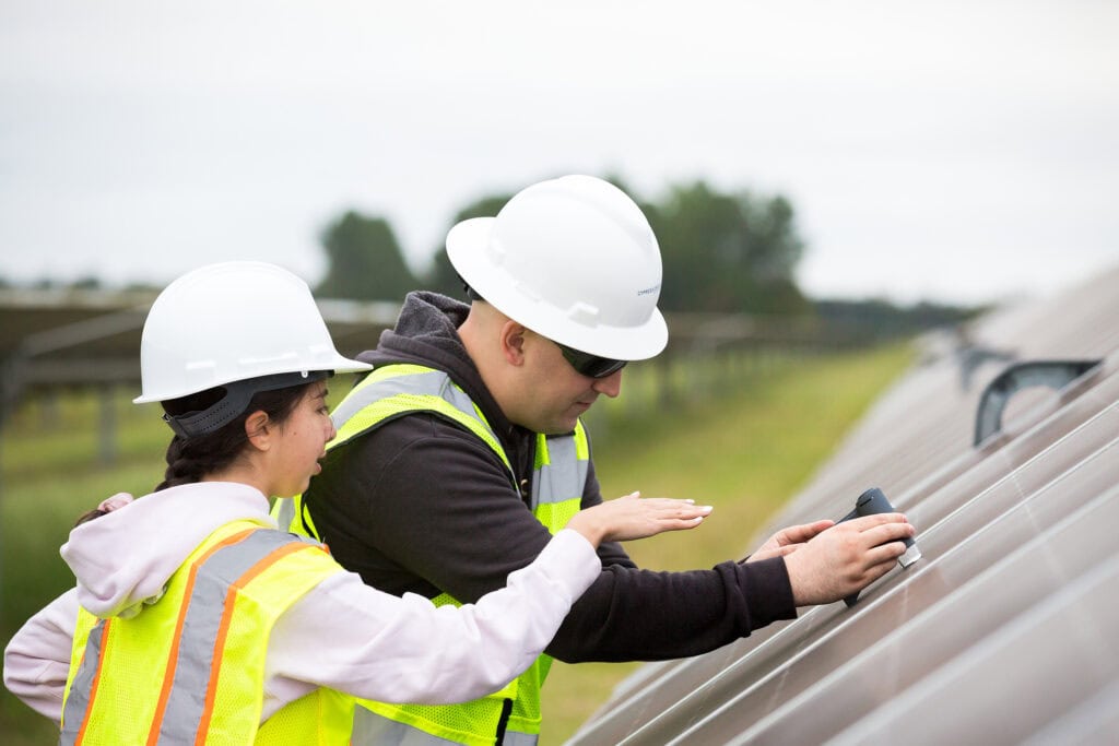 A man and a woman use a device to look at the cells of a solar panel