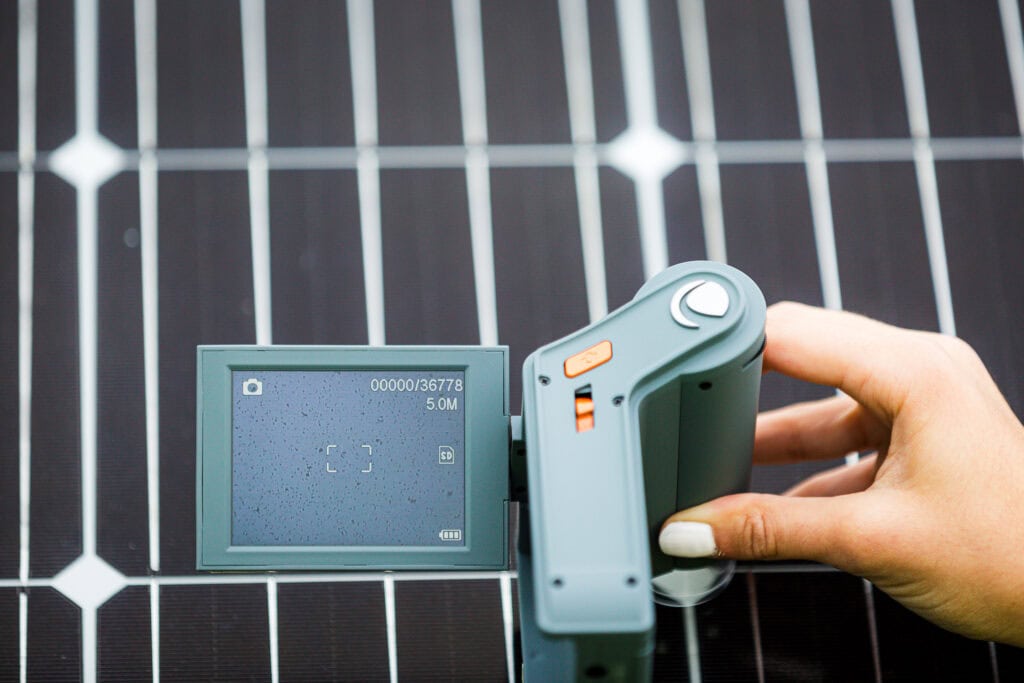 A woman holds a device to measure soiling up to a solar panel