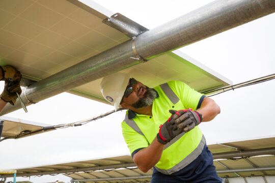 A man in a hardhat looks under a solar panel