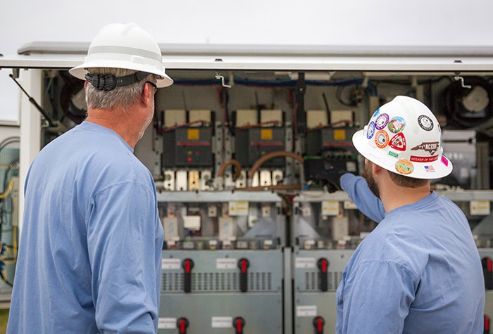 two men are seen from behind as they look at an open inverter